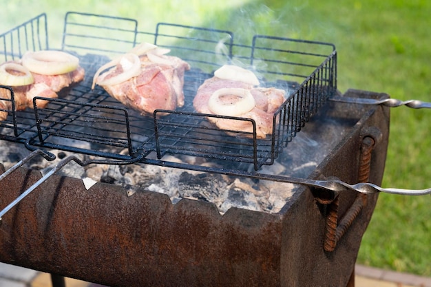 la carne se cocina en una parrilla de carbón caliente hay humo en el fondo un césped verde