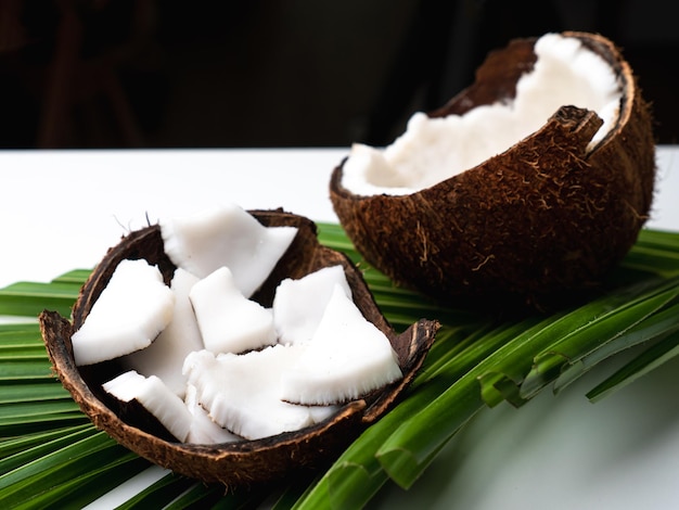 Carne de coco y hoja de coco en mesa blanca.