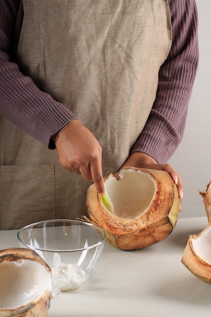 Carne de coco joven desmenuzada a mano femenina en el cuenco, preparación para hacer Es Kelapa Muda (hielo de coco joven) para el desayuno de Ramadán