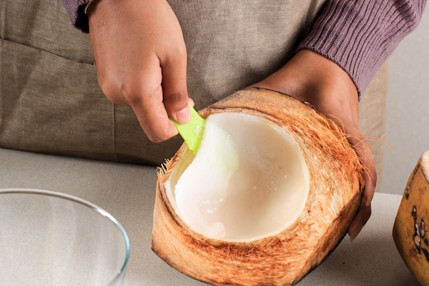 Carne de coco joven desmenuzada a mano femenina en el cuenco, preparación para hacer Es Kelapa Muda (hielo de coco joven) para el desayuno de Ramadán