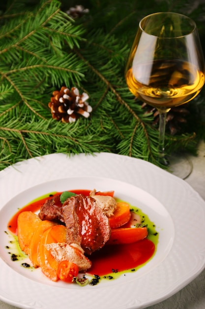 Carne com caqui e copo de vinho branco na árvore de natal. carne recheada com frutas.