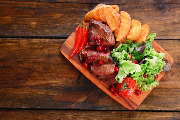 Carne com molho de cranberry fatias de batata assada na tábua sobre fundo de madeira