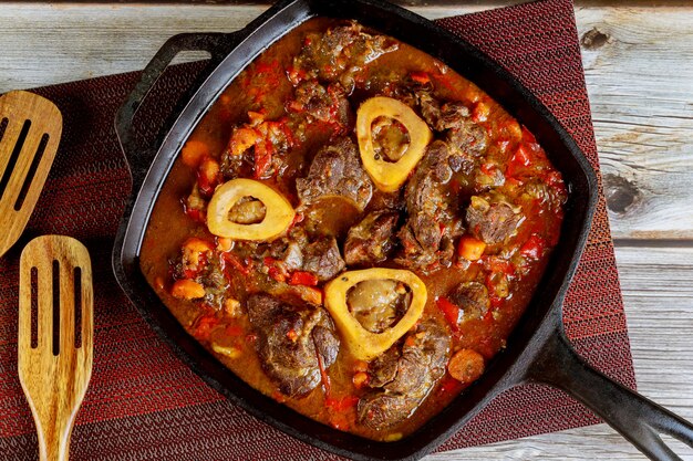 Carne com osso estufado em frigideira de ferro com cenoura, cebola e pimentão vermelho.