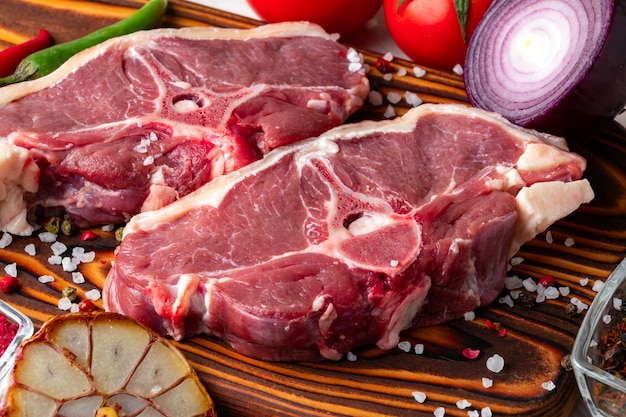 Carne de cordero cruda en una tabla de cortar de madera con especias y verduras frescas