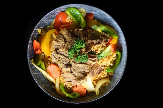 Carne cozida com macarrão e legumes em uma tigela azul isolada na vista superior de fundo preto