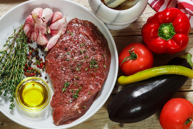 Carne crua com especiarias e tomilho e legumes frescos em cima da mesa