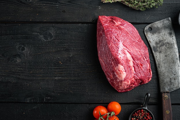 Carne crua cortada com faca de cutelo de açougueiro, no fundo preto da mesa de madeira, vista de cima plana, com espaço de cópia para o texto