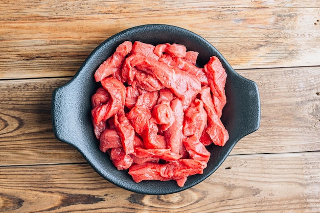 Carne crua crua cortada em tiras com ingredientes para estrogonofe de carne sobre fundo de madeira rústico