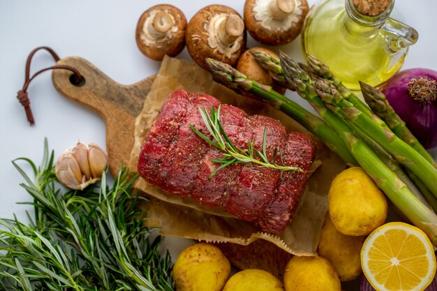 Carne crua de carne vermelha com alecrim verde e legumes frescos em uma tábua de madeira