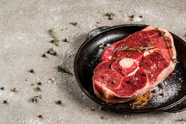 Carne crua fresca. Um pedaço de lombo de cordeiro, com um osso, com um machado de corte, com especiarias para cozinhar na mesa de pedra cinza