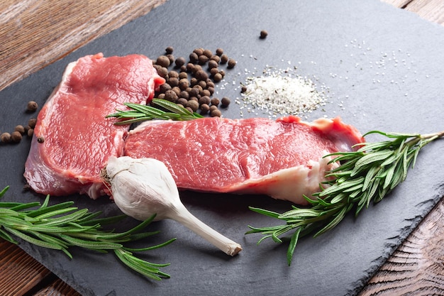 Carne cruda y ajo Rodajas de ajo de carne cruda fresca y una rama de romero sobre una piedra de pizarra negra