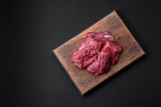 Carne cruda cortada en varios pedazos en una tabla de cortar de madera sobre un fondo de hormigón oscuro