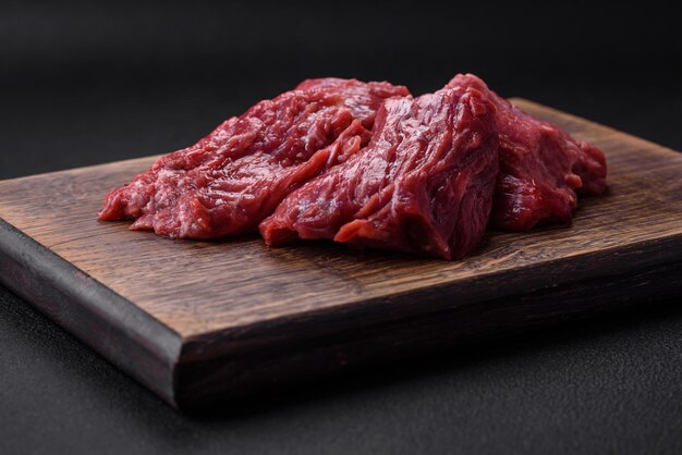 Carne cruda cortada en varios pedazos en una tabla de cortar de madera sobre un fondo de hormigón oscuro