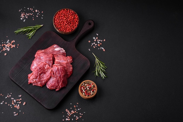 Carne cruda cortada en varios pedazos en una tabla de cortar de madera sobre un fondo de hormigón oscuro