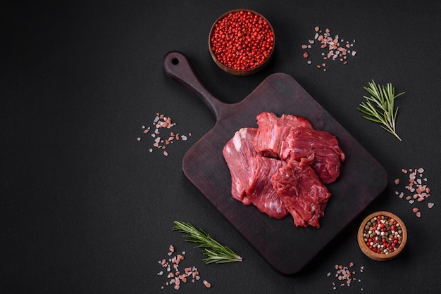 Carne cruda cortada en varios pedazos en una tabla de cortar de madera sobre un fondo de hormigón oscuro