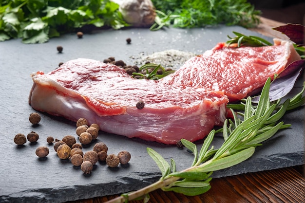 Carne cruda con especias Dos rebanadas de carne cruda fresca, sal, pimienta y romero sobre una piedra de pizarra negra