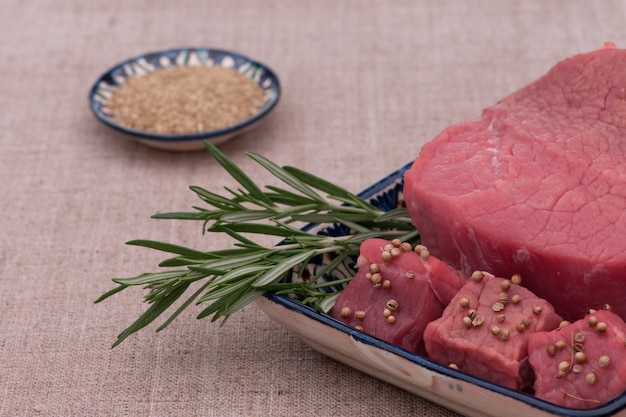 Carne cruda con especias y hierbas en un plato cuadrado sobre un tejido con textura