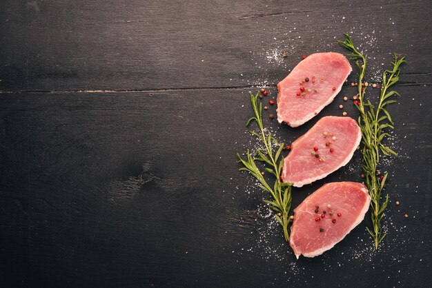 Carne cruda Filete de ternera con romero y especias sobre un fondo de madera negra Vista superior Espacio libre para texto