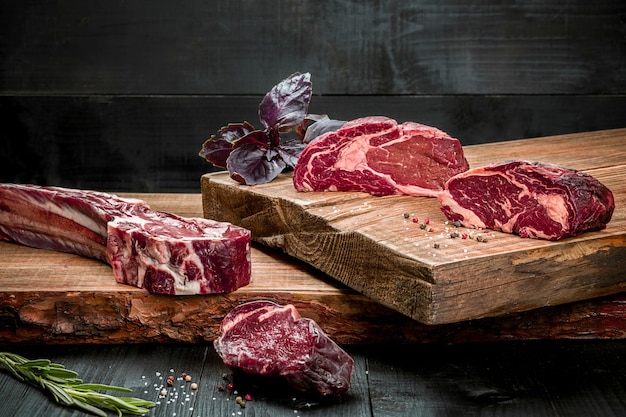 Carne cruda fresca sobre tabla de cortar con especias, albahaca fresca y una ramita de romero sobre un fondo de madera. Carne de vacuno de marmol envejecido en seco