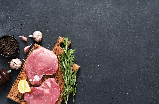 Carne cruda fresca sobre una tabla de madera con romero y limón sobre un cerdo de fondo negro