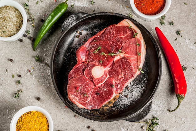 Carne cruda fresca. Un trozo de lomo de cordero, con un hueso, con un hacha cortante, con especias para cocinar sobre la mesa de piedra gris Vista superior