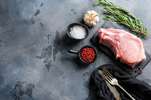 Carne cruda con hierbas y especias en pizarra negra sobre fondo gris