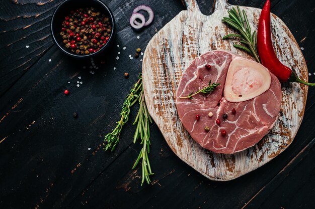 Carne cruda de mármol de bistec Ossobuko con hierbas y especias en el menú de banner de fondo oscuro lugar de recetas para la vista superior de texto