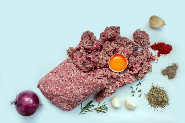 Carne cruda picada con pimienta, huevo, hierbas y especias para cocinar chuletas, hamburguesas, albóndigas. Concepto- cocina, recetas, platos deliciosos. Copia espacio