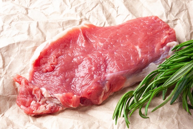 Carne cruda Rebanada de carne cruda fresca con romero en papel Preparando carne para una barbacoa