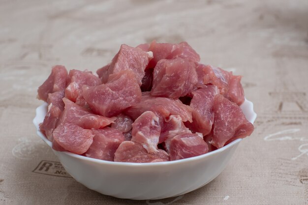 Carne cruda en rodajas en un recipiente blanco sobre una mesa de luz. Vista desde arriba.