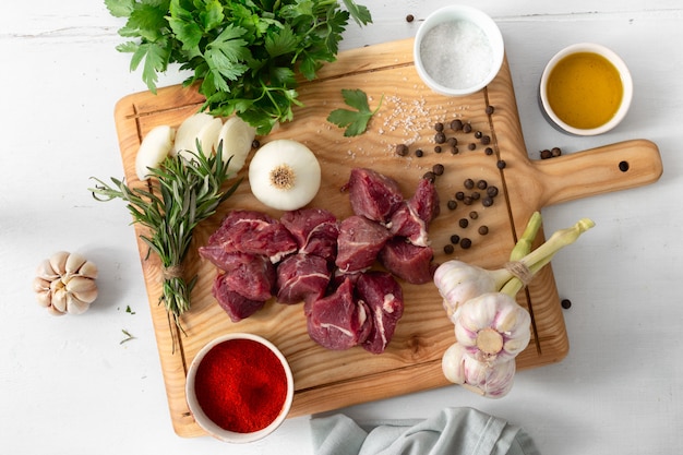 Carne cruda y verduras en la vista superior del tablero de madera blanca. Cocinar carne de res