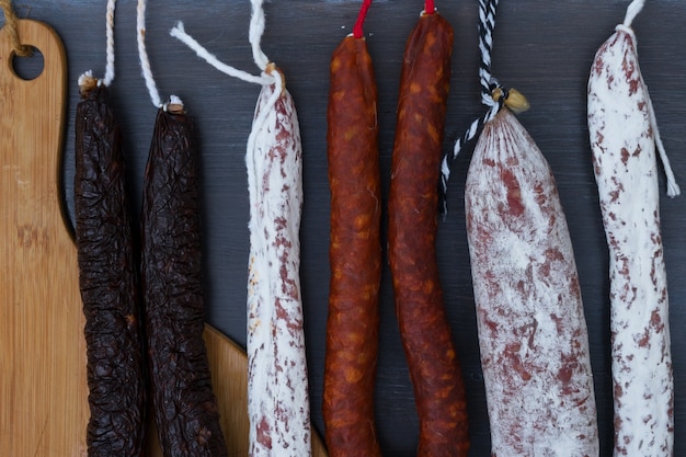 Carne curada e salsichas penduradas em um fundo preto de madeira close-up