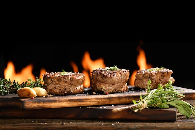 Carne de carne suculenta cozida com tempero na tábua de madeira com chamas ao fundo