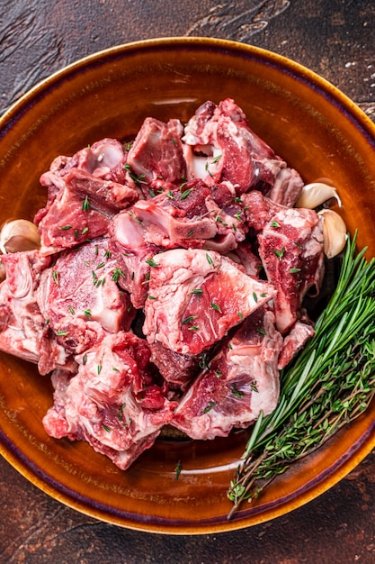 Carne de carneiro crua em cubos para goulash ou guisado com osso em prato rústico. Fundo escuro. Vista do topo.