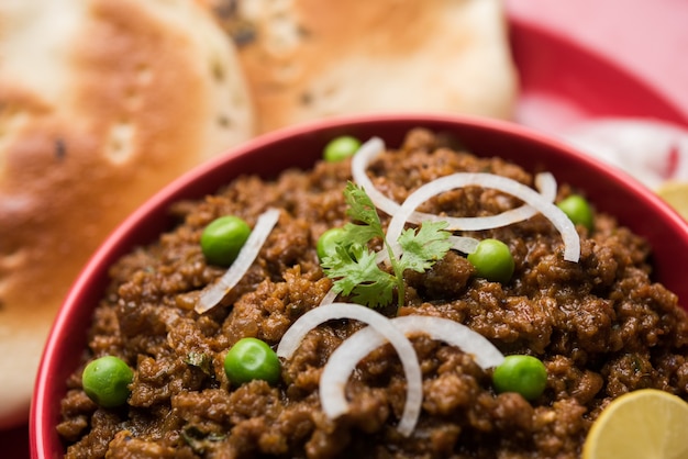 Carne de carneiro Kheema Pav OU carne picada picante indiana servida com pão OU kulcha, guarnecida com ervilhas verdes. Fundo temperamental. Foco seletivo