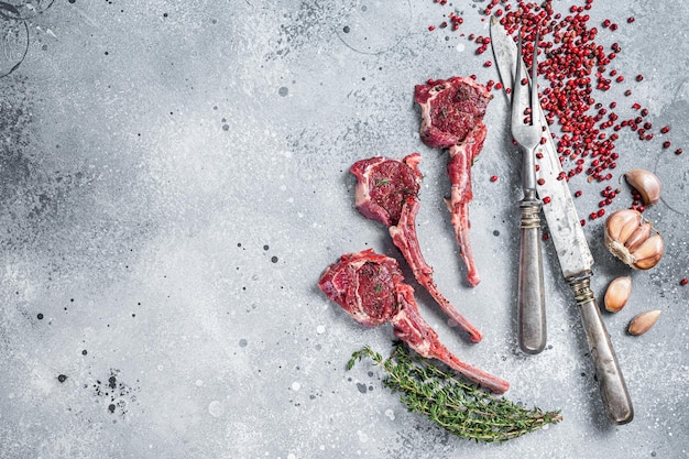 Carne de cordeiro crua corta bifes em uma mesa de açougueiro com pimenta e tomilho. Fundo cinza. Vista do topo. Copie o espaço.