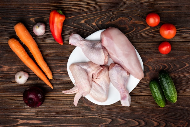 Carne de frango cru na madeira escura com legumes.