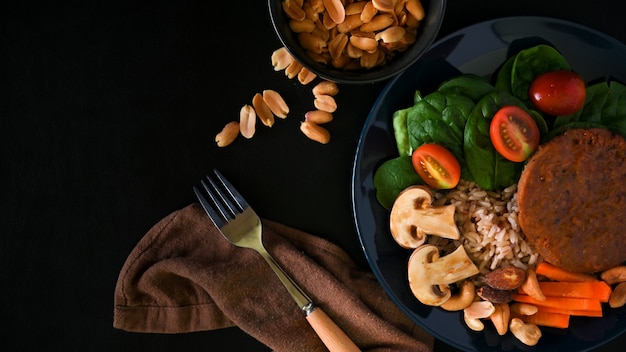 Carne de hambúrguer à base de vegetais com arroz integral, uma tigela de nozes e copie o espaço no fundo preto