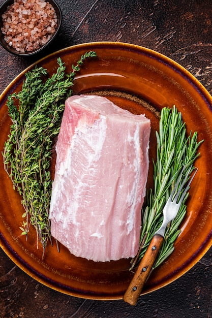 Carne de lombo de porco crua fresca com tomilho e alecrim no prato rústico.