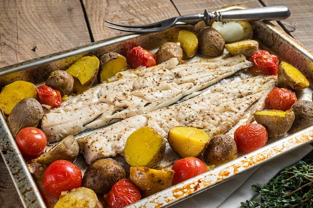 Foto carne de peixe assado filé de pescada com tomate e batata fundo de madeira vista superior