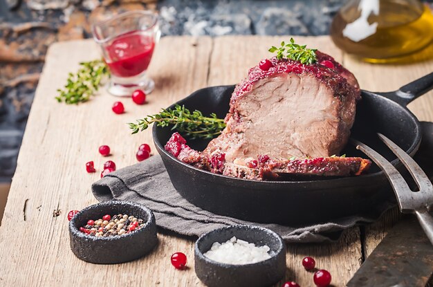 Carne de porco assada com molho de cranberry e tomilho sobre a superfície de madeira - conceitos de comida festiva