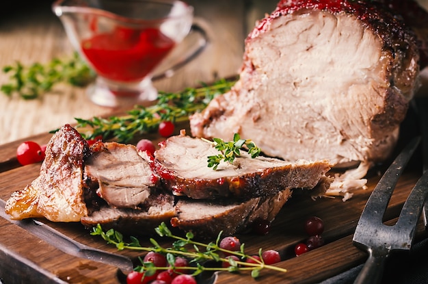 Carne de porco assada com molho de cranberry e tomilho sobre a superfície de madeira - conceitos de comida festiva