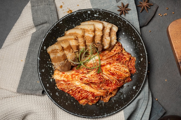 Carne de porco cozida coreana com preparação de kimchi de repolho em prato preto. Cozinha tradicional coreana. Alimentos fermentados.