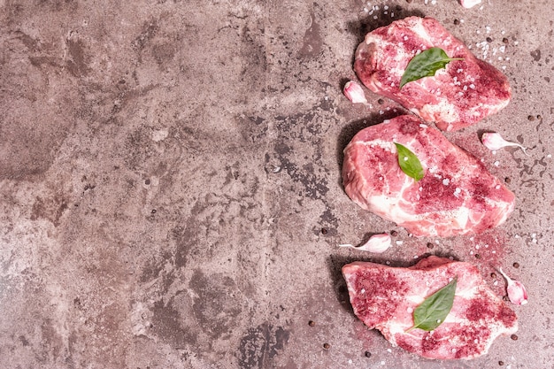 Carne de porco crua, cortes fatiados. Carne fresca, sumagre seco, alho e folhas de manjericão. Conceito de comida de culinária saudável, luz dura na moda, sombra escura. Fundo de pedra de mármore, vista superior