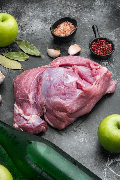 Carne de porco crua e ingredientes para assados, com cidra de maçã seca, no fundo da mesa de pedra escura preta