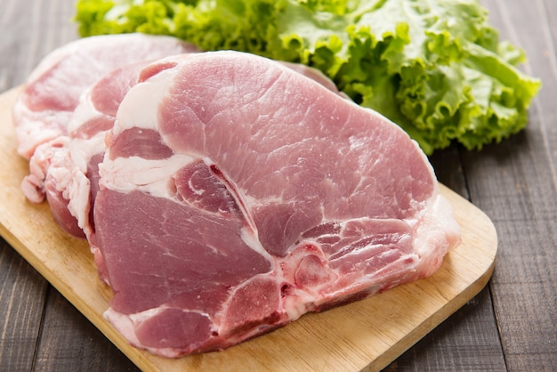 Carne de porco crua na tábua e legumes na mesa de madeira