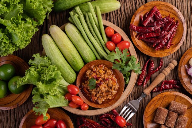 Foto carne de porco doce em uma tigela de madeira com pepino, feijão longo, tomates e acompanhamentos