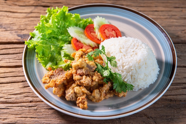 Foto carne de porco frita coberta com arroz, servido com alface, pepino, tomate, arrume um prato bonito, coloque sobre uma mesa de madeira.