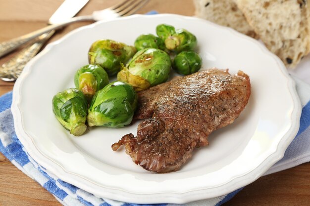 Carne e legumes assados no prato, no fundo da mesa de madeira