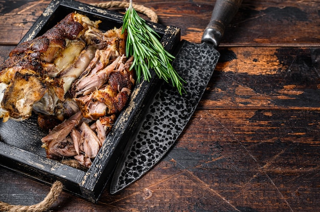 Carne de eisbein de codillo de cerdo asado en una bandeja de madera con cuchillo. Fondo de madera oscura. Vista superior. Copie el espacio.